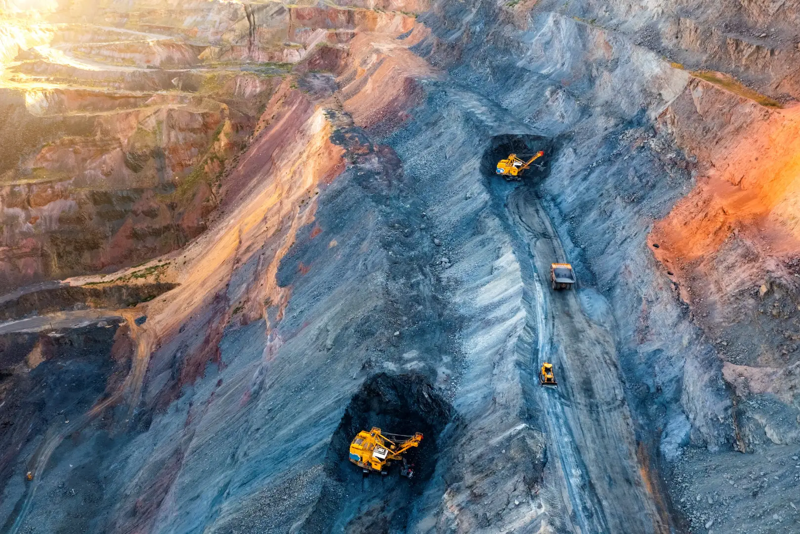 A wide-angle shot of a mining site with large excavators digging and moving earth in a multi-layered excavation area.